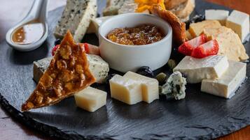 Una variedad de quesos y frutas sobre una tabla de pizarra, con un recipiente de chutney y una cuchara.