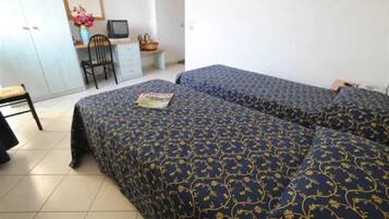 Ein Zimmer mit zwei Betten, einem Schreibtisch mit Computer, einem Stuhl und einem kleinen Tisch mit einem Korb.