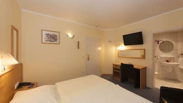 Habitación de hotel con cama, mesita de noche, escritorio, silla, televisor y baño con lavamanos e inodoro.