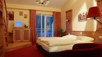Ein Hotelzimmer mit einem Bett, einem Schreibtisch mit Computer, einem roten Sessel, einer roten Lampe und einem Balkon mit Vorhängen.