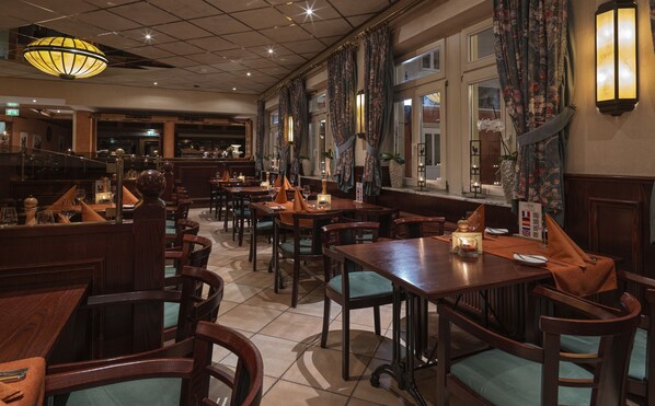 Un restaurante con mesas y sillas de madera, una zona de bar e iluminación decorativa.