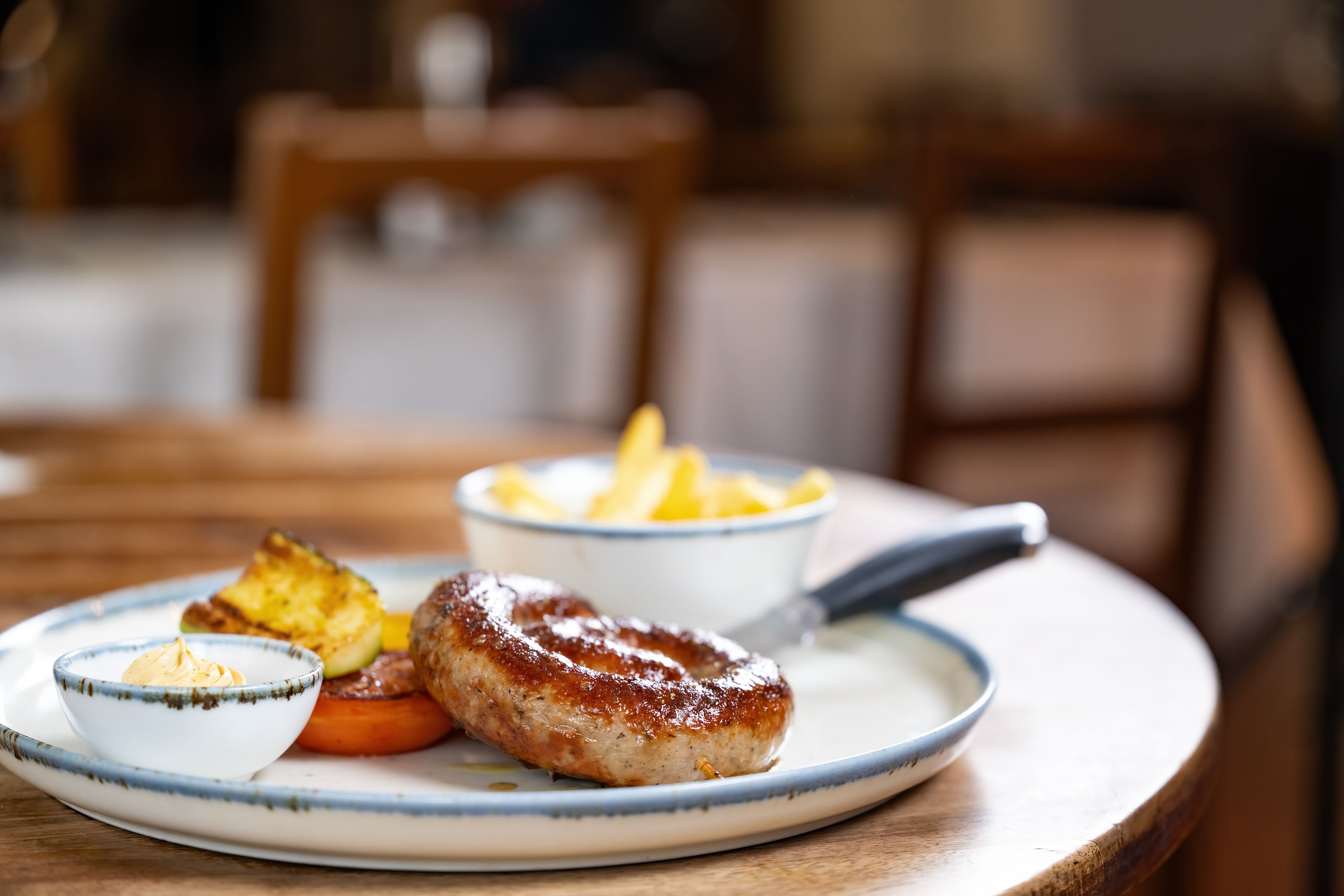 Une assiette avec une viande grillée, un petit bol de sauce et un bol de frites, le tout posé sur une table ronde.