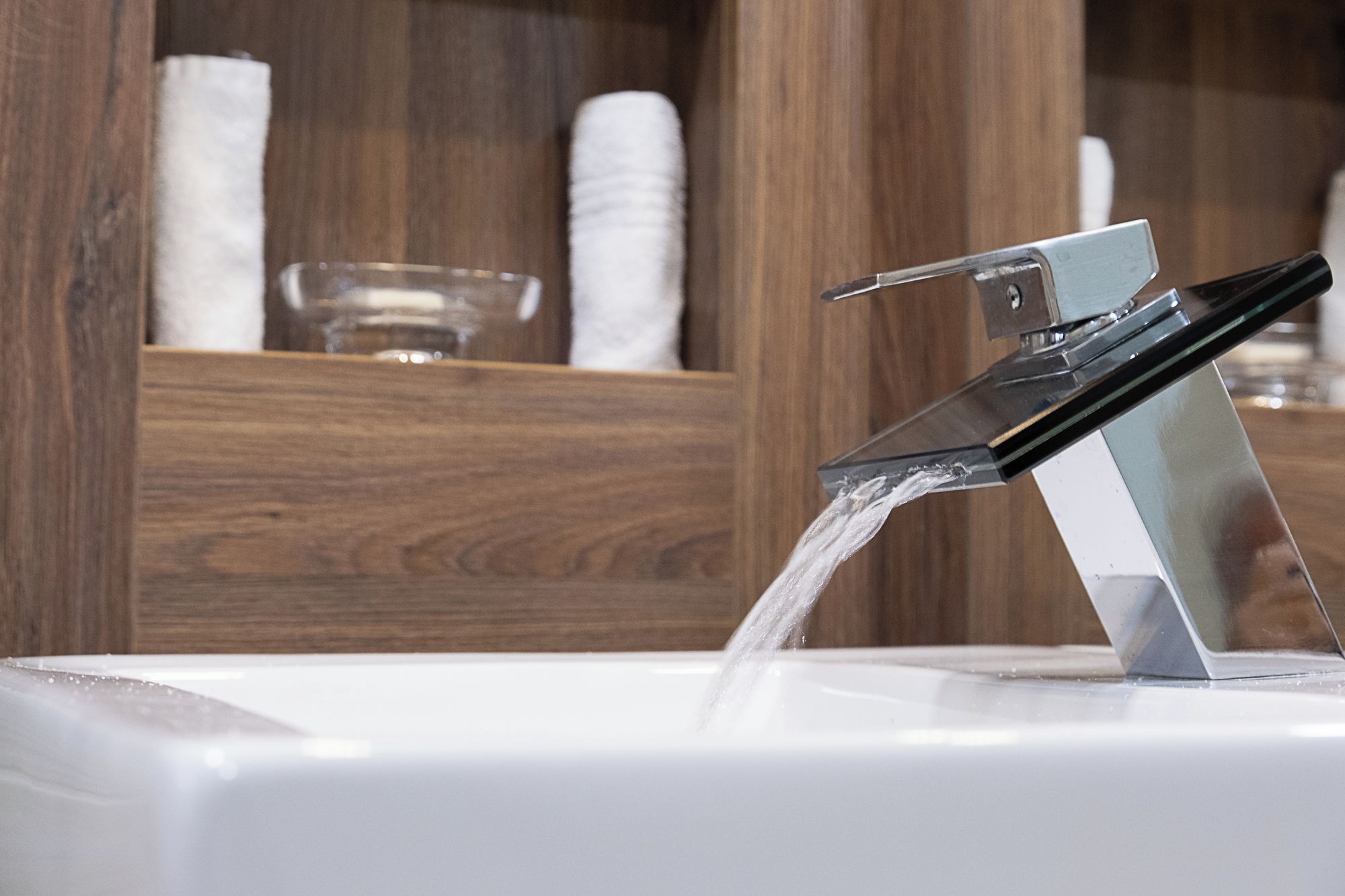 Un baño moderno con un grifo de cristal transparente sobre un lavabo blanco.