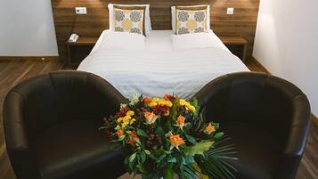 Una habitación de hotel con una cama grande, dos mesitas de noche, un escritorio con un florero y dos sillones.