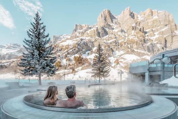 A hot spring with two people enjoying the view of snow-covered mountains. - Hotel Römerhof (Leukerbad)