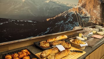 Un buffet proposant une variété de pains et de viennoiseries, un présentoir de fromages et une vue imprenable sur les montagnes en arrière-plan.