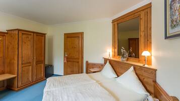 A bedroom with a large bed, wooden wardrobe, a desk with a lamp, and a mirror above the bed.