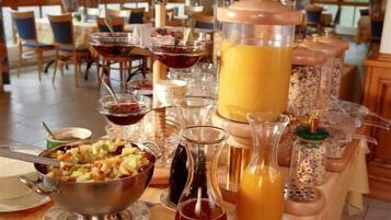 A buffet table with various food items and beverages, including a large pitcher of orange juice, a bowl of fruit salad, and several condiment containers.