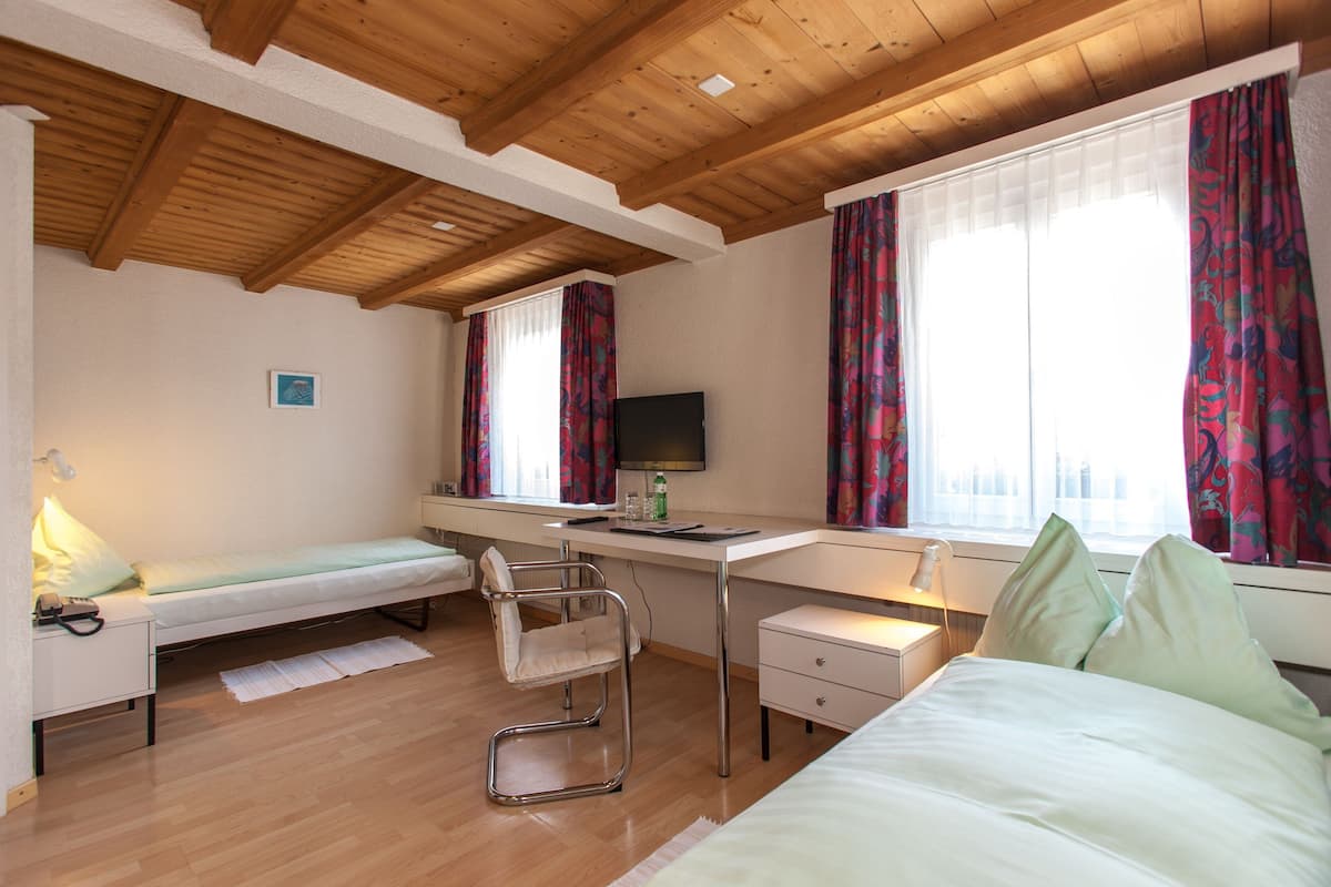 A compact bedroom with a bed, a desk, a chair, and a TV.