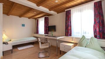 A compact bedroom with a bed, a desk, a chair, and a TV.