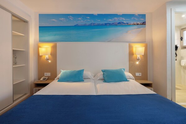 A hotel room with a bed, two bedside lamps, a painting of a beach, and a telephone on the nightstand. - whala!beach Hotel & Apartments (Llucmajor)