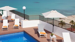 Zona junto a la piscina con sillones de descanso y sombrillas, con vistas a una playa y al océano.