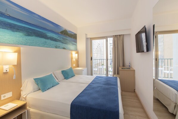 Habitación de hotel con dos camas, un cuadro de una escena costera, un escritorio con lámpara y un balcón con una silla.