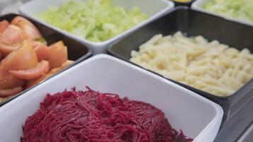Un bufé con distintos alimentos, entre ellos tomates en rodajas, remolacha rallada y otras verduras.