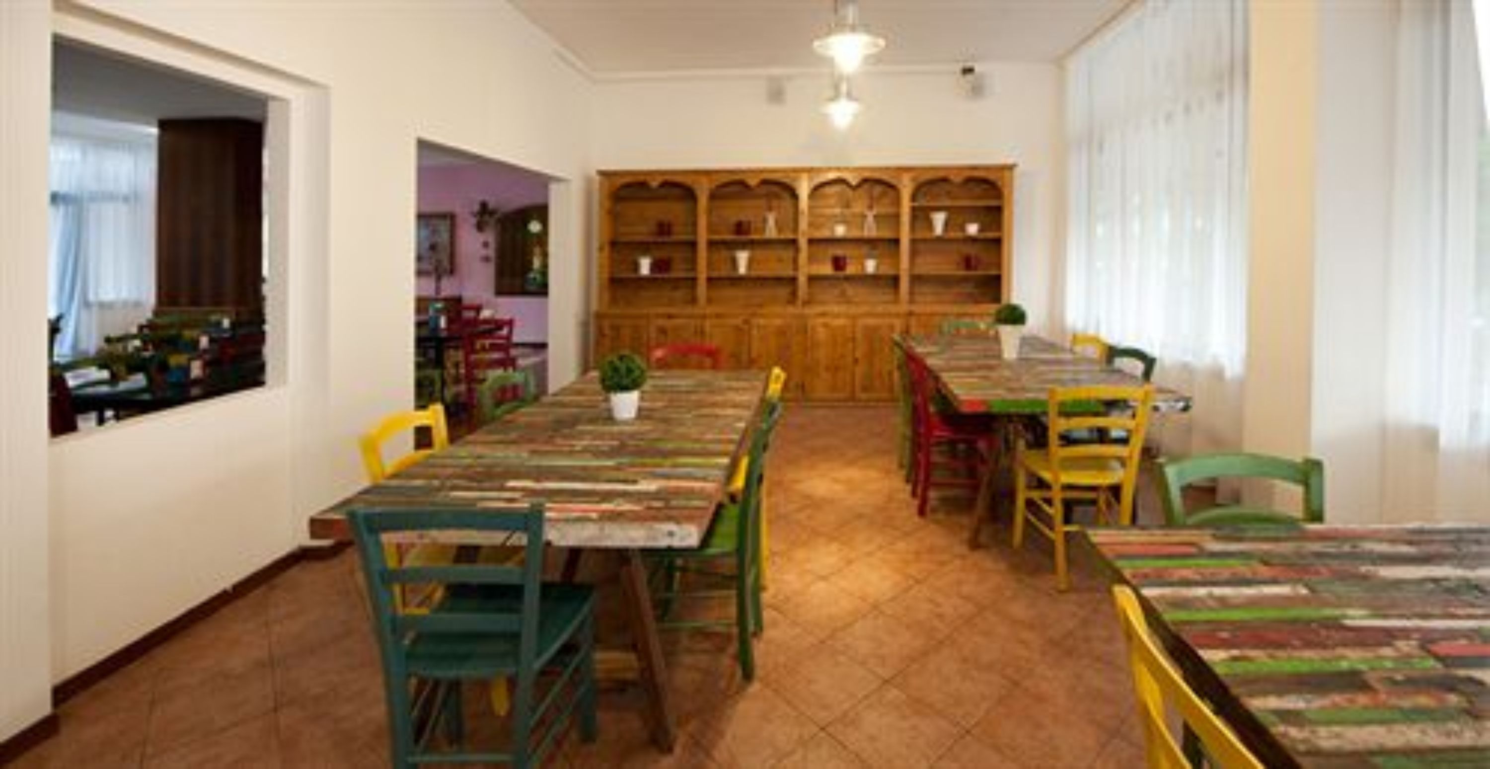 A dining area with a long table, multiple chairs, and a wooden bookshelf in the background.