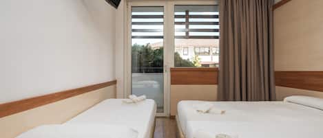 A hotel room with two beds, a sliding glass door to the balcony, and a TV mounted on the wall.