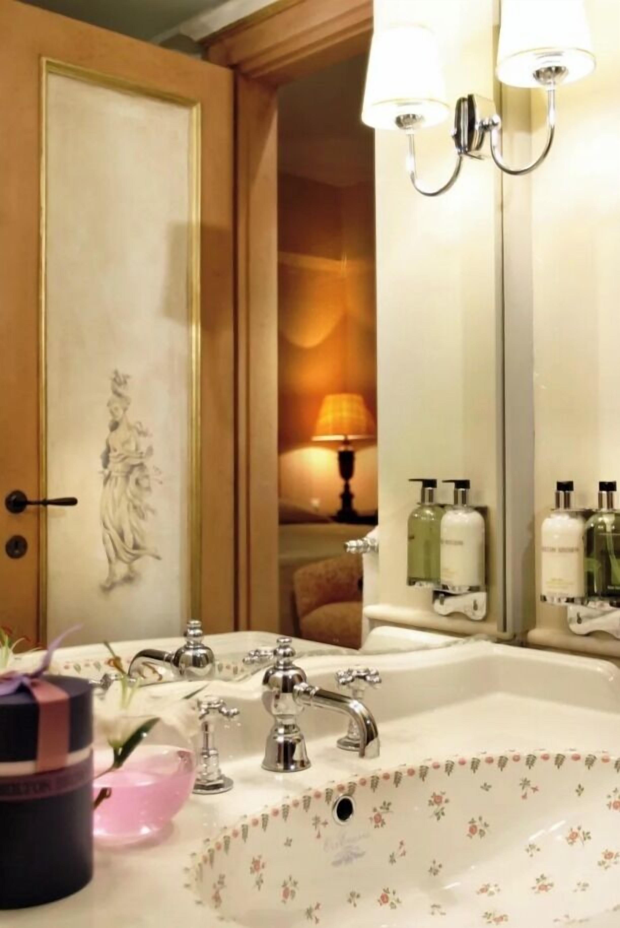 A bathroom with a sink, two wall-mounted lights, a mirror, and a door with a decorative panel.