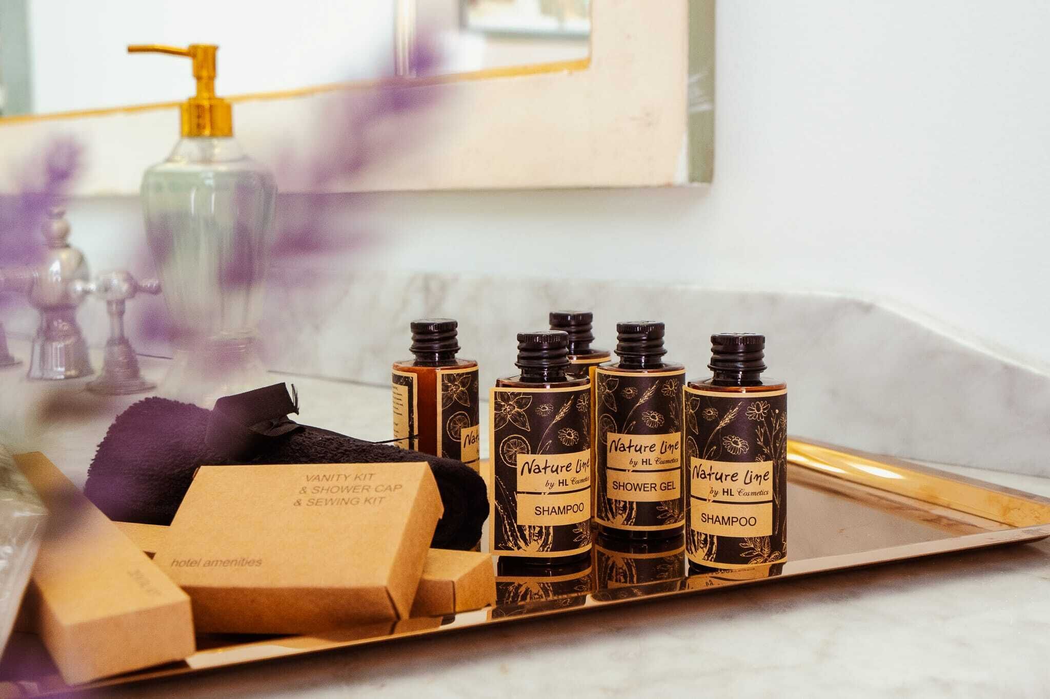 A bathroom vanity with a mirror, a soap dispenser, and a tray holding bottles of shampoo and shower gel.