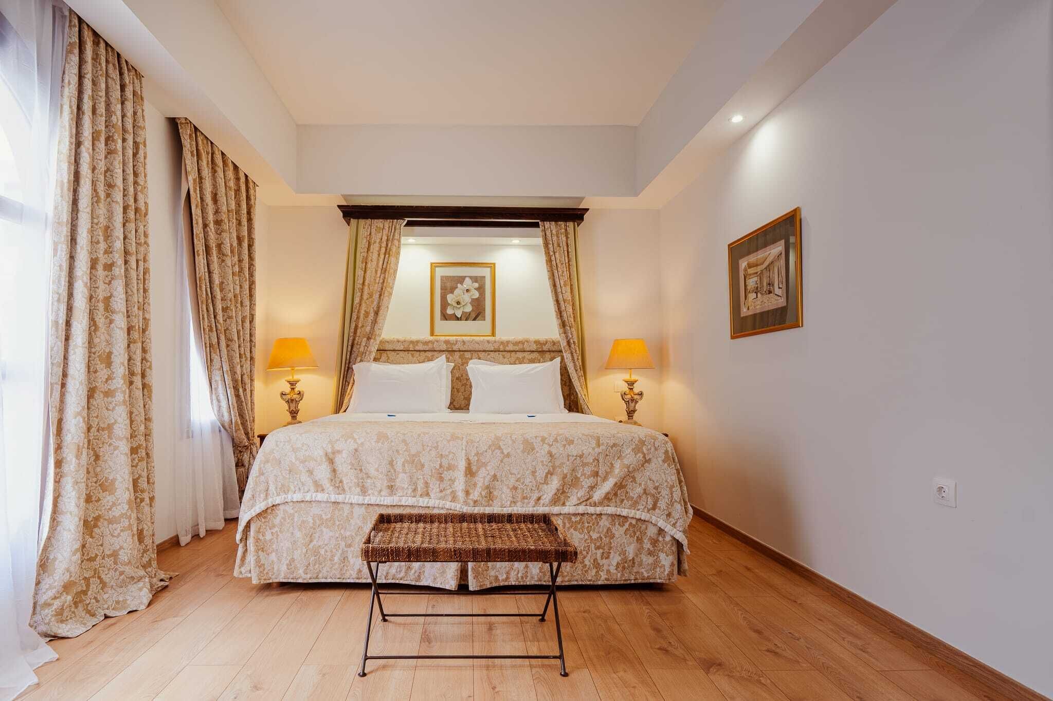 Un dormitorio con cama, dos lámparas de noche, un cuadro en la pared y un banco frente a la cama.