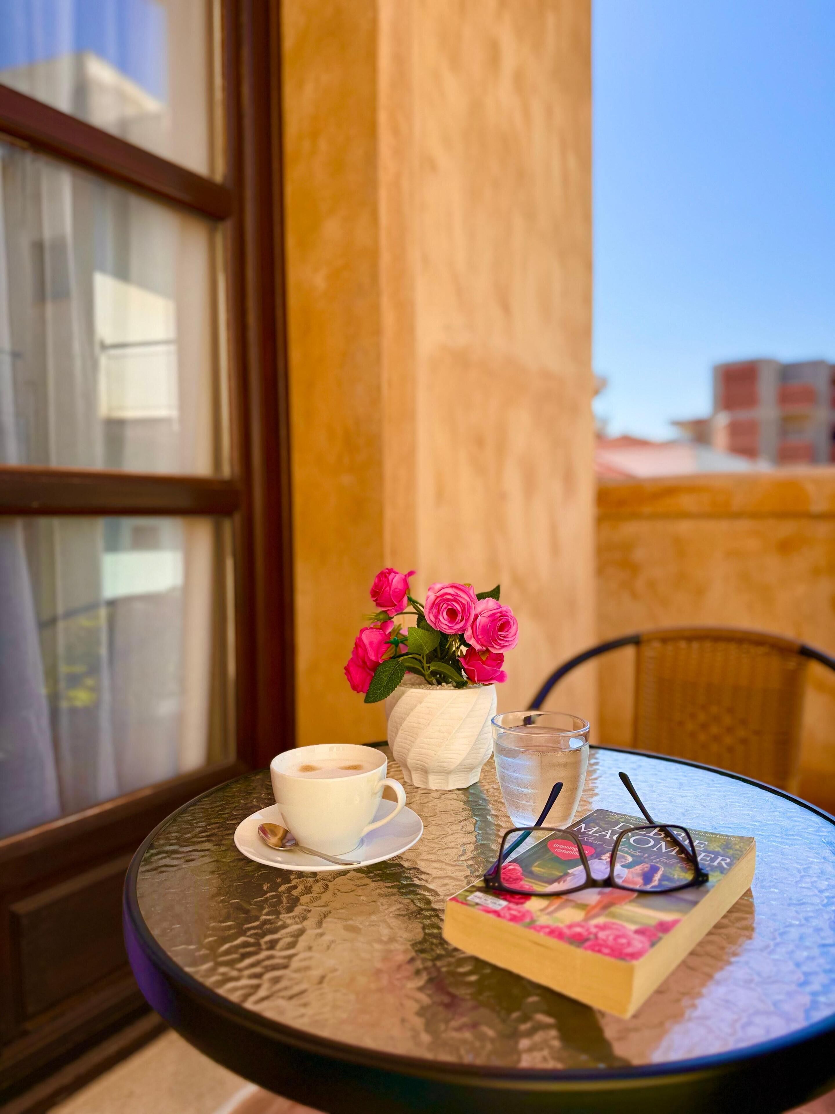 Une table ronde avec une tasse blanche, un verre d’eau, un livre et une paire de lunettes.