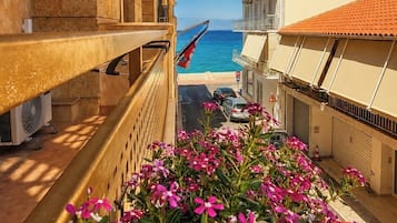 Un balcón con vista al mar, un edificio con balcones y un jardín con flores rosas.