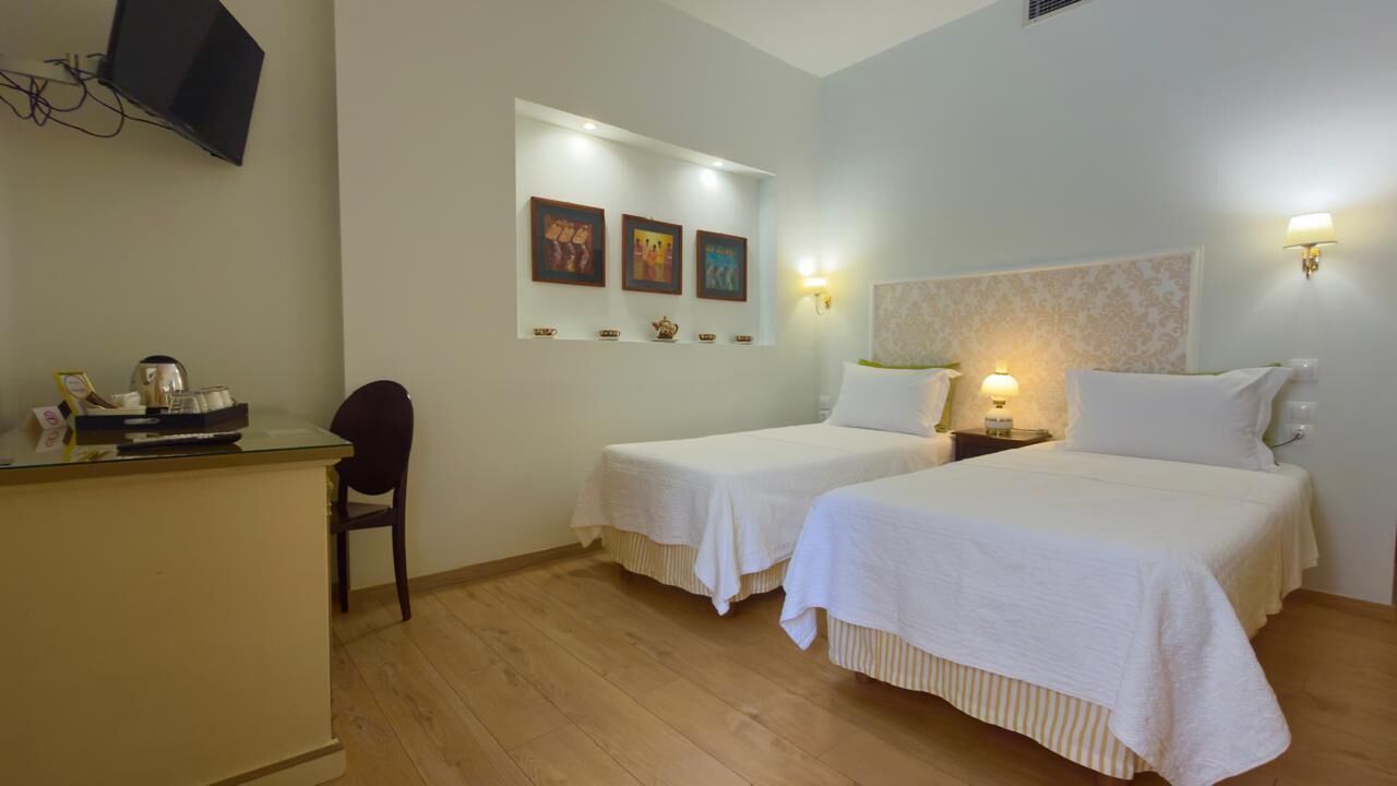 Une chambre d’hôtel avec deux lits, un bureau, une chaise et des œuvres d’art accrochées au mur.