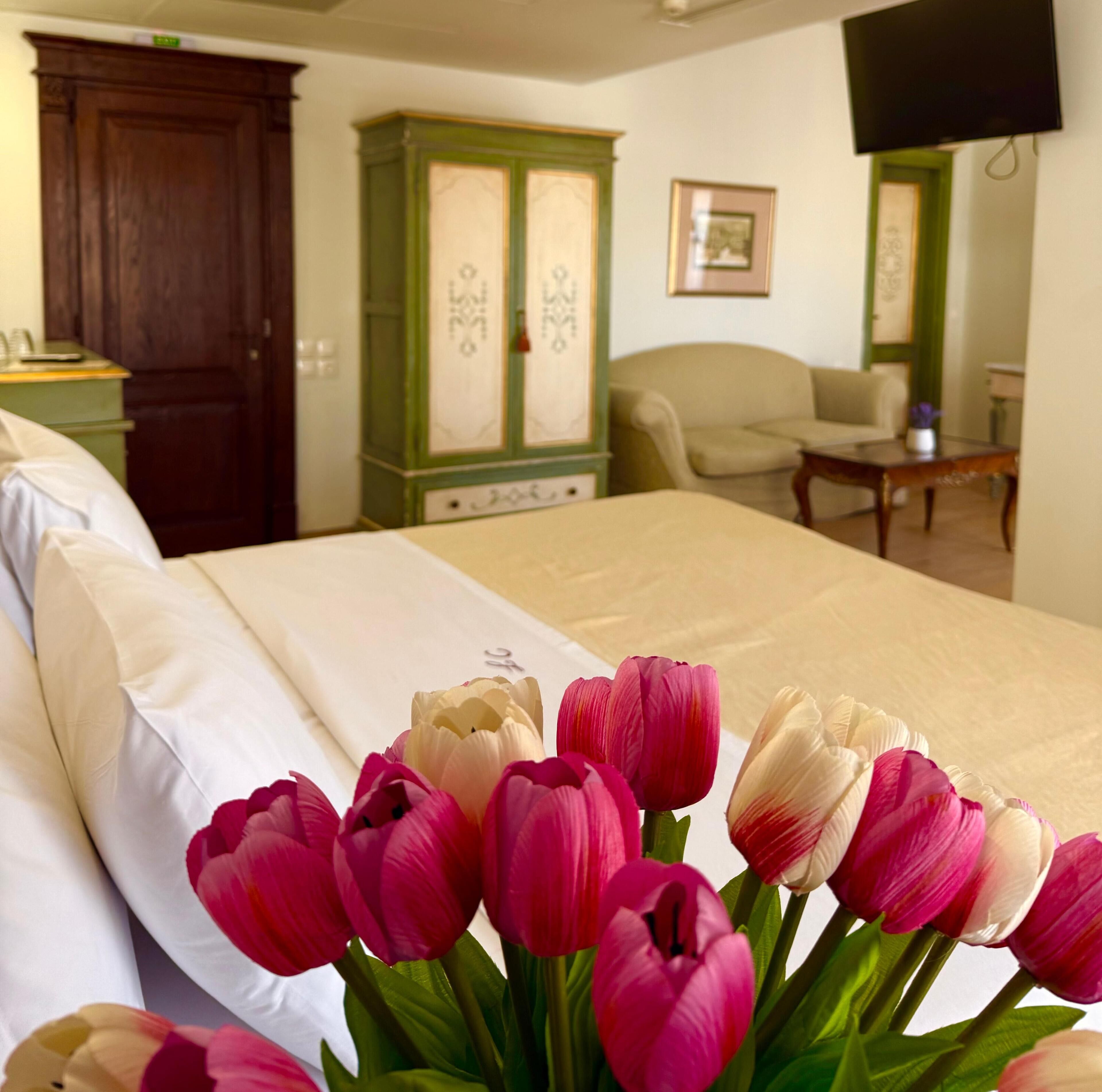 A hotel room with a bed, a green cabinet, a chair, a table, and a TV mounted on the wall.