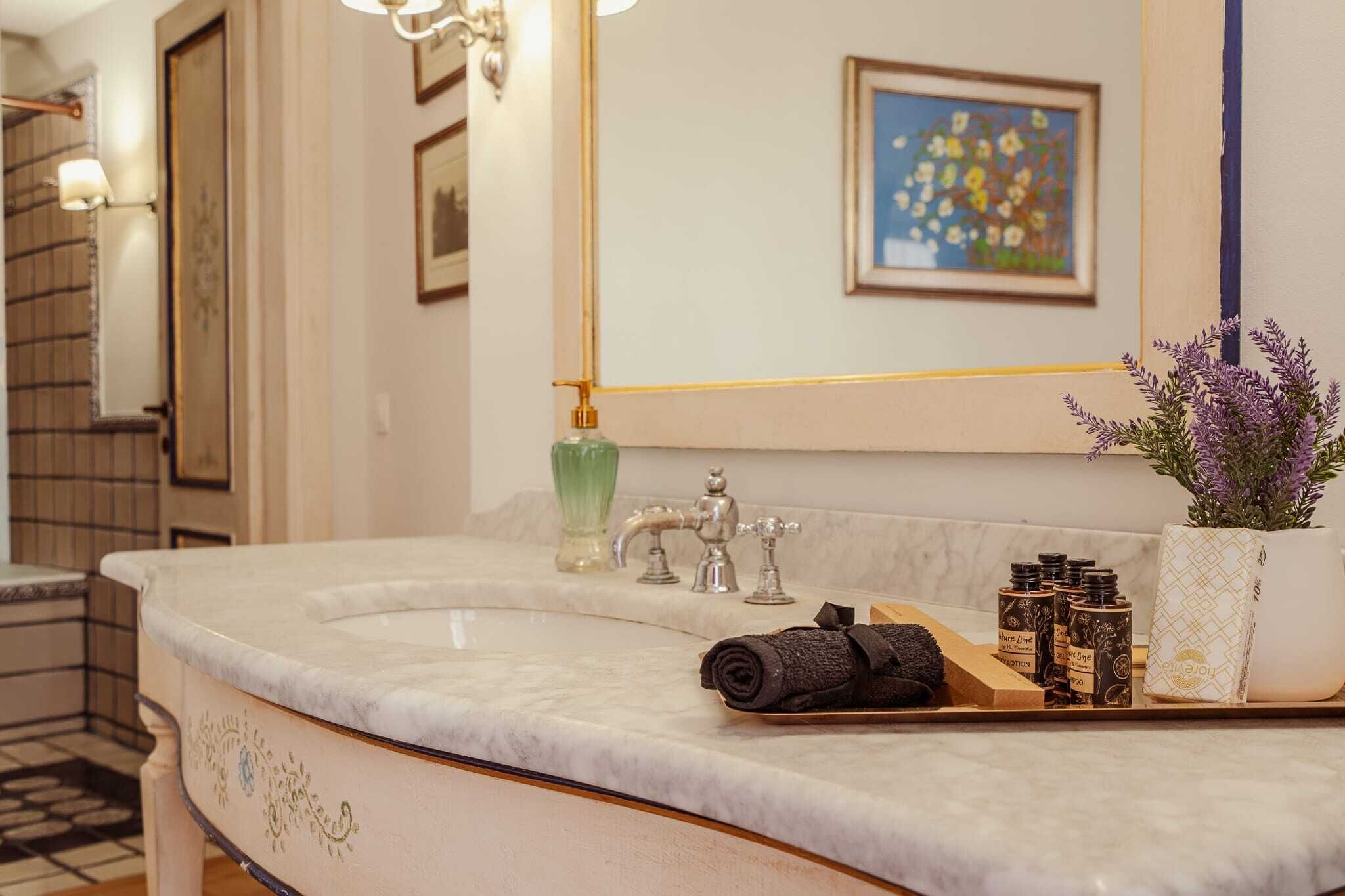 A bathroom with a marble sink, a green soap dispenser, a lavender plant, and a towel.
