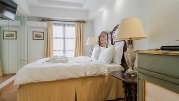 Habitació d'hotel amb llit, taulells laterals, una petarrera, un mirall i una finestra amb cortines.
