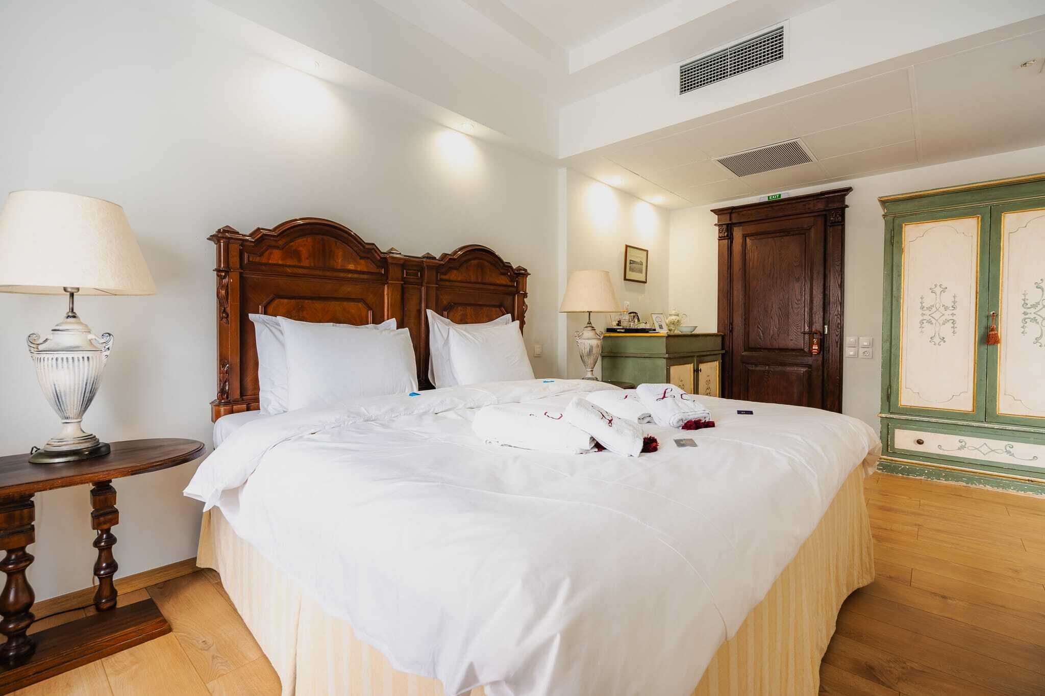 Un letto rifatto con lenzuola bianche, una testiera in legno, un comodino con una lampada e un armadio con cornice verde.