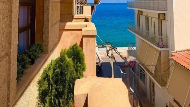 A narrow urban street with a building featuring a large arched window and a balcony overlooking a clear blue sea. - Great Greece Le Convivial Suites & Spa (Xylokastro-Evrostina)