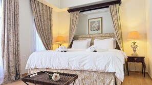 Quarto de hotel com uma cama grande, mesa de cabeceira com abajur, moldura decorativa e cesta de vime com uma flor.