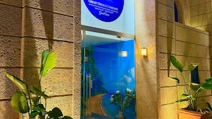 The entrance of the Great Greece Company hotel with a stone facade, a blue sign, and potted plants. - Great Greece Le Convivial Suites & Spa (Xylokastro-Evrostina)