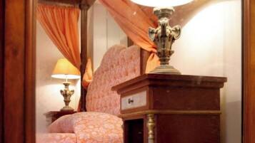 A mirror reflecting a room with a bed, a nightstand, and a lamp.