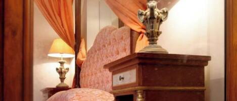 A mirror reflecting a room with a bed, a nightstand, and a lamp.