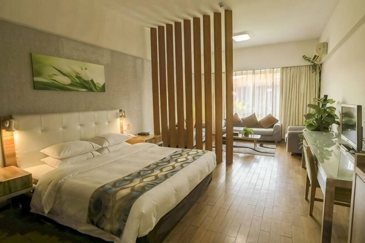 A hotel room with a bed, bedside tables, a desk, a chair, a TV, and a large window.