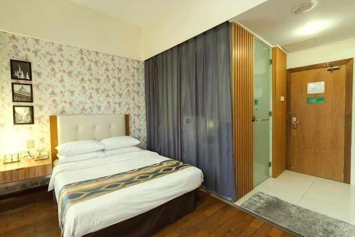 A hotel room with a bed, a nightstand, a wall clock, and a door with a sign.