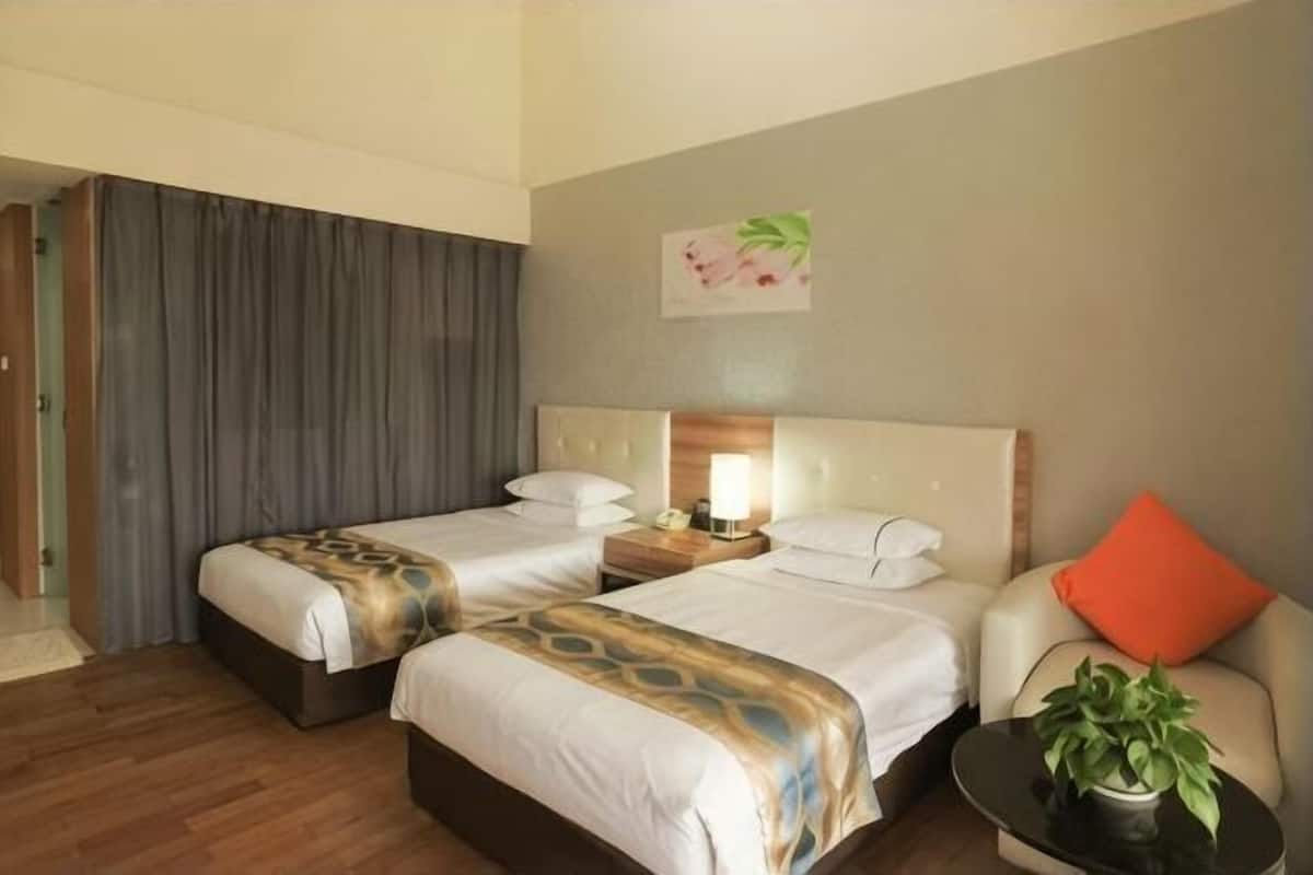 A hotel room with two beds, a nightstand, a lamp, a potted plant, and a painting on the wall.