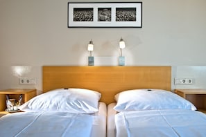 Ein Doppelbett mit weißen Bettwäsche, zwei Nachttische mit Lampen, ein gerahmtes Foto über dem Bett und ein Holzkopfschild.