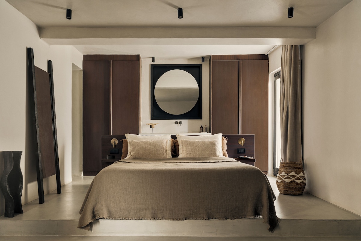 A bedroom with a large bed, a round mirror, and wooden wardrobes.