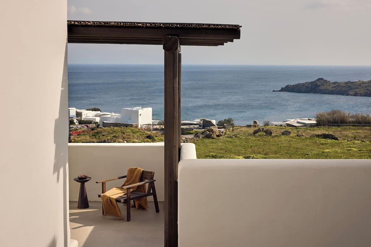 A balcony with a view of the sea, a chair, a small table, and a pergola.