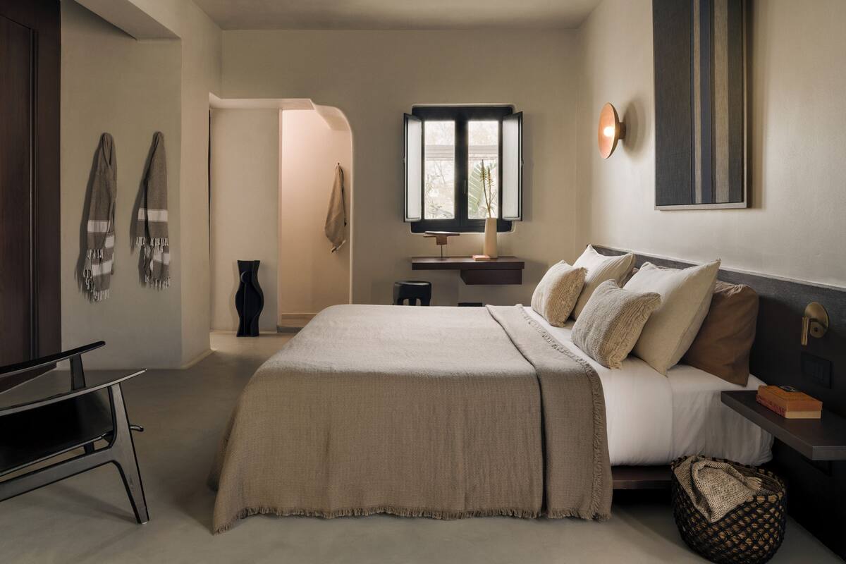A bedroom with a bed, bedside table, lamp, and a window.