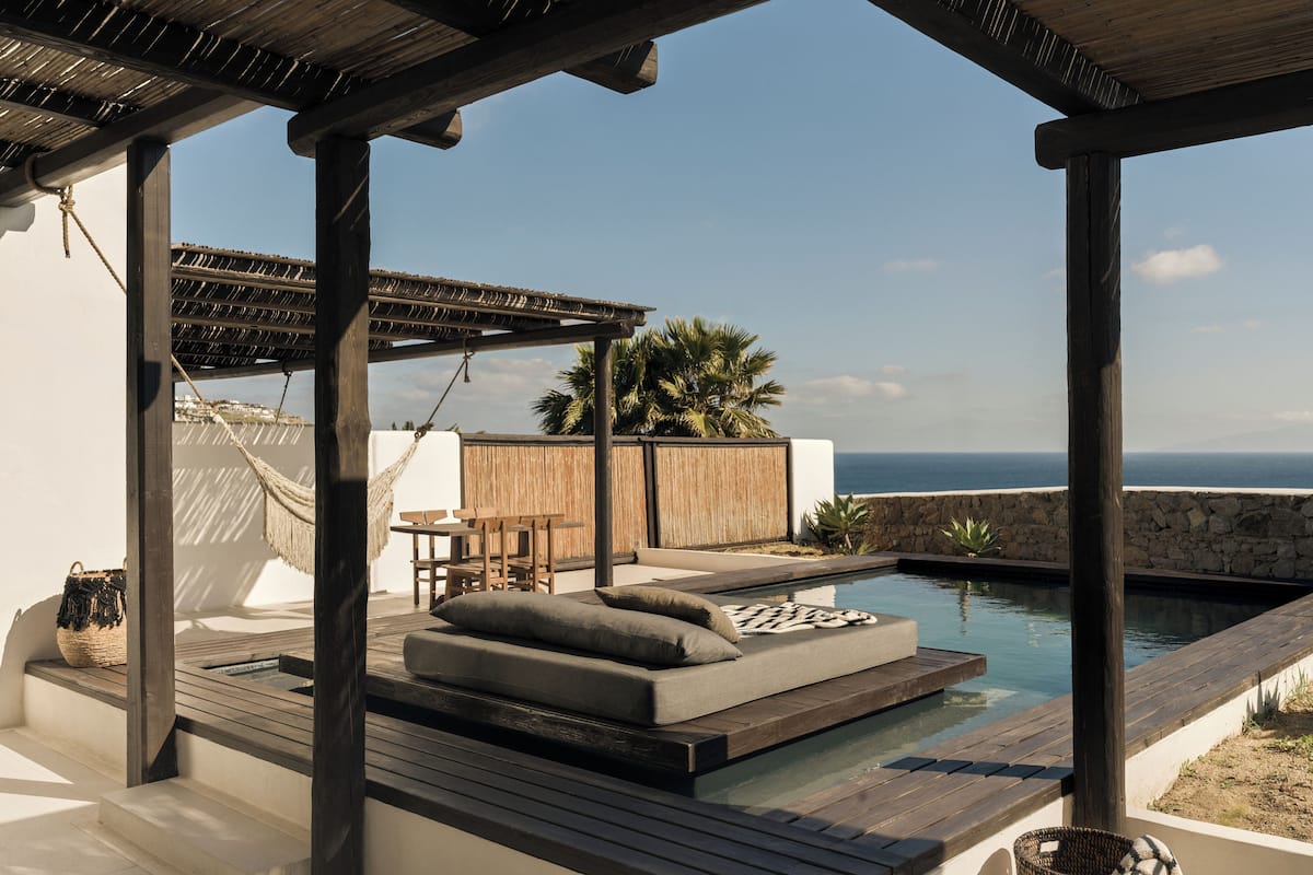 A rooftop pool area with a wooden deck, seating, and a view of the ocean.