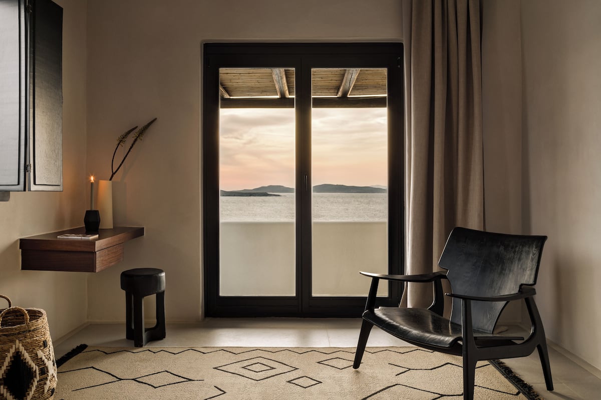 A room with a view of the sea, a chair, a small table with a candle, and a rug.