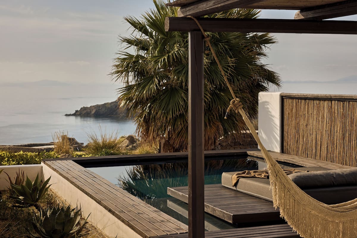 A pool area with a hammock, wooden deck, and a view of the sea.