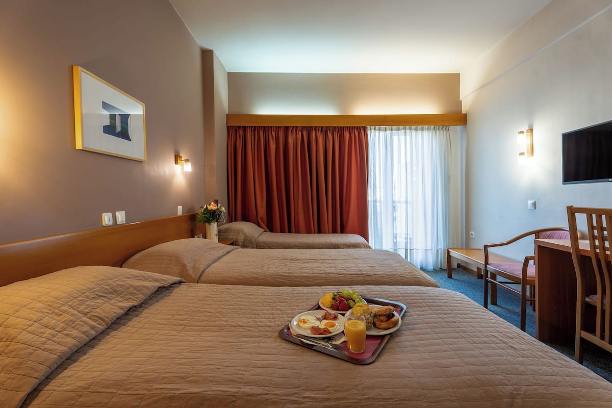 A hotel room with two beds, a desk, and a chair. There is a tray with breakfast items on the bed.