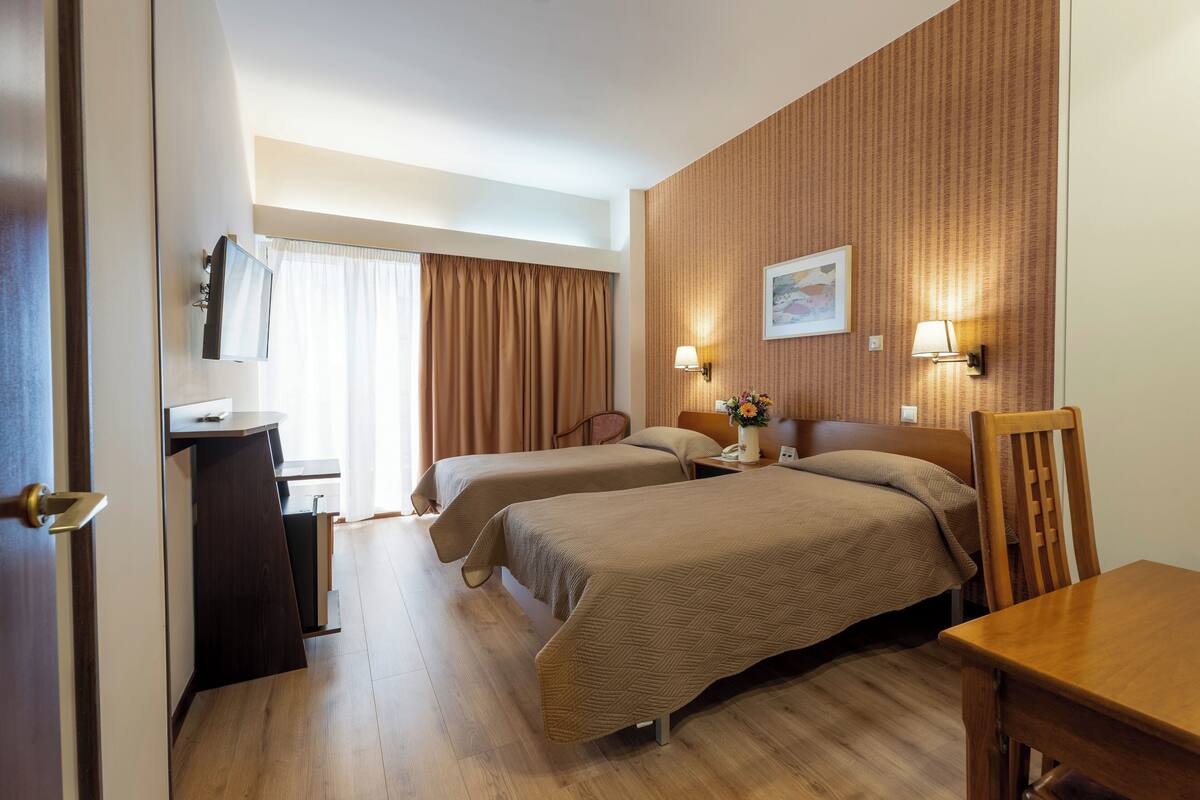 A hotel room with two beds, a desk, a chair, a lamp, and a painting on the wall.