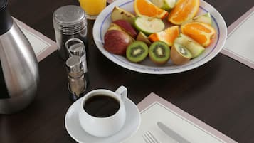 Un desayuno con una bandeja de fruta, una taza de café y un termo sobre una mesa de madera.