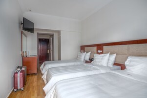 Quarto de hotel com duas camas, cabeceira de madeira, televisão na parede e mala no chão.