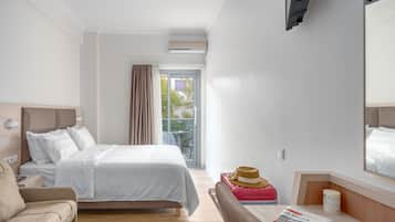 Habitación de hotel con cama, una silla, una mesa con una revista, ventana con cortinas y un espejo en la pared.